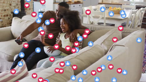 animation of social media icons over african american father and daughter watching tv