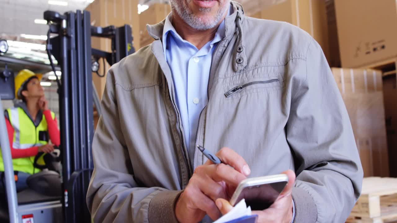 Warehouse manager entering stock data via stylus animating charts while forklift placing load