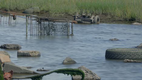 rusty trash shopping cart and old tyre plus rubble with tide rising and cloud to sunshine breaks