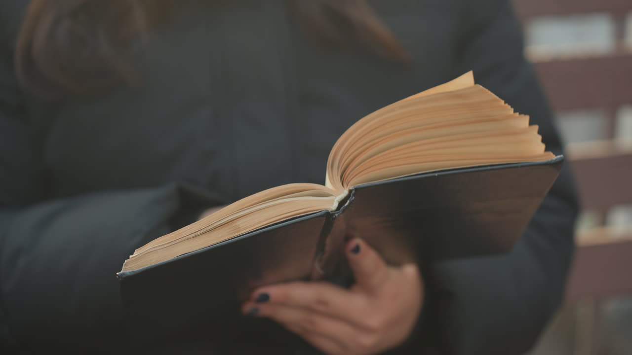 Lettura in città. Studente che sfoglia le pagine attentamente. Studente concentrato che legge pagine all'aperto in ambiente urbano. Studente che si concentra sulla lettura di pagine su una panchina in un contesto urbano soffuso.