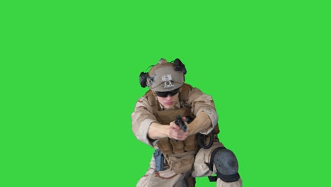 soldier is shooting with hand pistol sitting on his knee on a green screen, chroma key