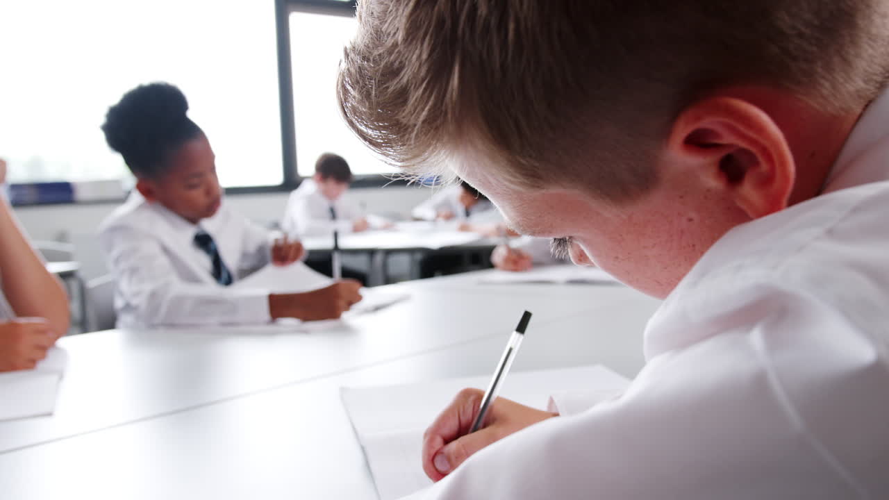 Group Of High School Students Wearing Uniform Working At Desks In Classroom