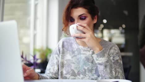 mujer hermosa sentada cerca de la ventana en una cafetería bebiendo café y trabajando en una computadora portátil. chica navegando por internet