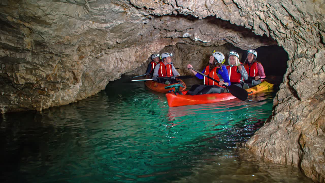 Friends exploring underground caves by kayak. Pristine emerald water