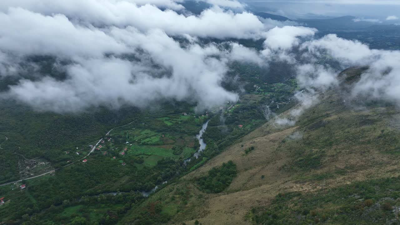 Mountain slopes and green valley with drifting clouds near Cetinje, Montenegro. Aerial pan left