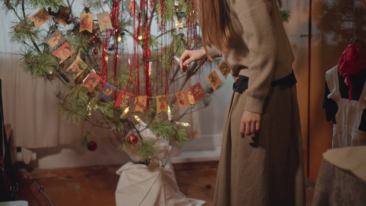 Joven seleccionando adornos navideños. Mujer arrodillada organizando cuidadosamente bolas festivas. Una joven con atuendo acogedor clasifica delicadamente adornos brillantes de una caja debajo del árbol de Navidad.