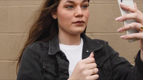 Steadicam-shot-of-a-beautiful,-young,-brunette-college-teenager-using-her-smart-phone-as-a-mirror-to-check-her-hair-and-makeup