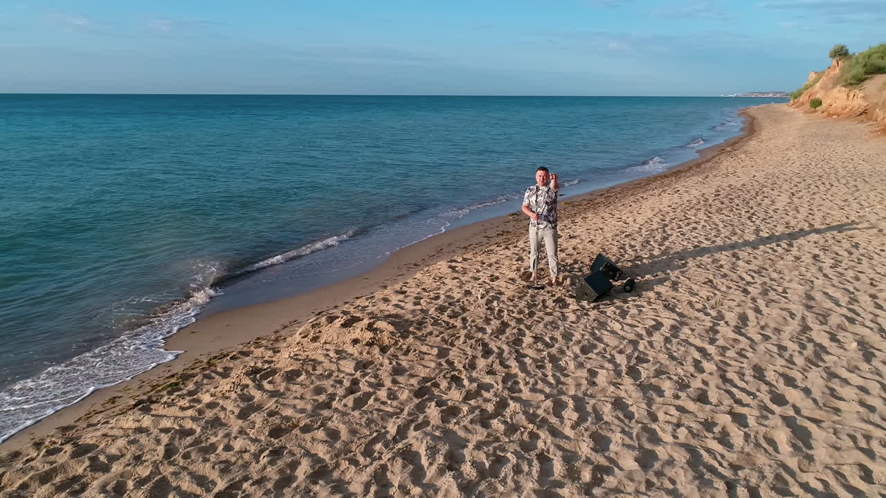 Male singer on a sea beach in summer. Musician standing on a sand shore and singing alone on a beautiful background of sea nature in sunny day.