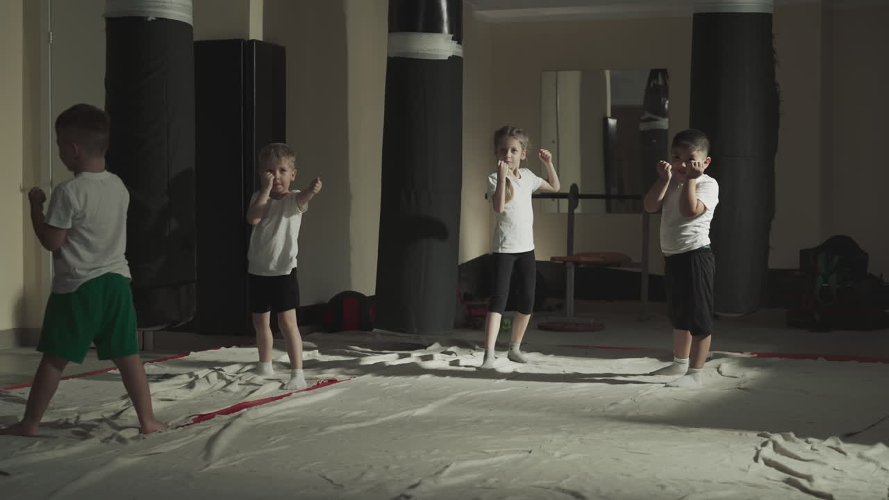 아이들은 무술 수업에서 전투자 위치에 서 있습니다. 작은 운동 선수 그룹은 체육관에서 느린 동작으로 전투 연습을 준비합니다.