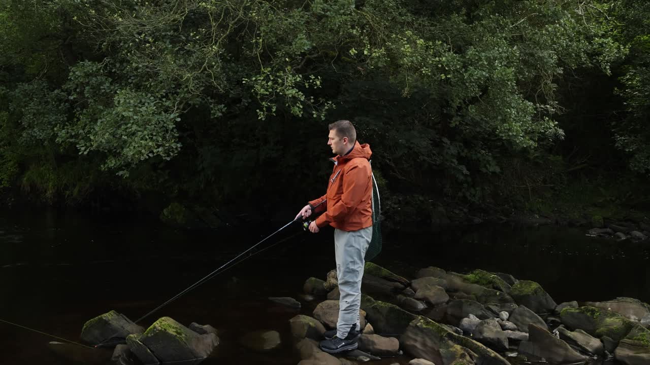 Rekaman genggam seorang pemancing yang melempar umpan pancing putarnya ke sungai kecil.