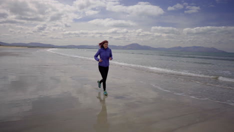 tracking dolly shot of a girl running, jogging on the shore of a sandy beach with atlantic ocean waves on a wonderful sunny day in ireland in 4k