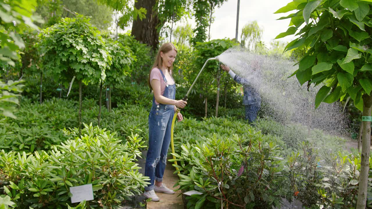 Um jardineiro e uma jardineira em pé, juntos, regando as flores.