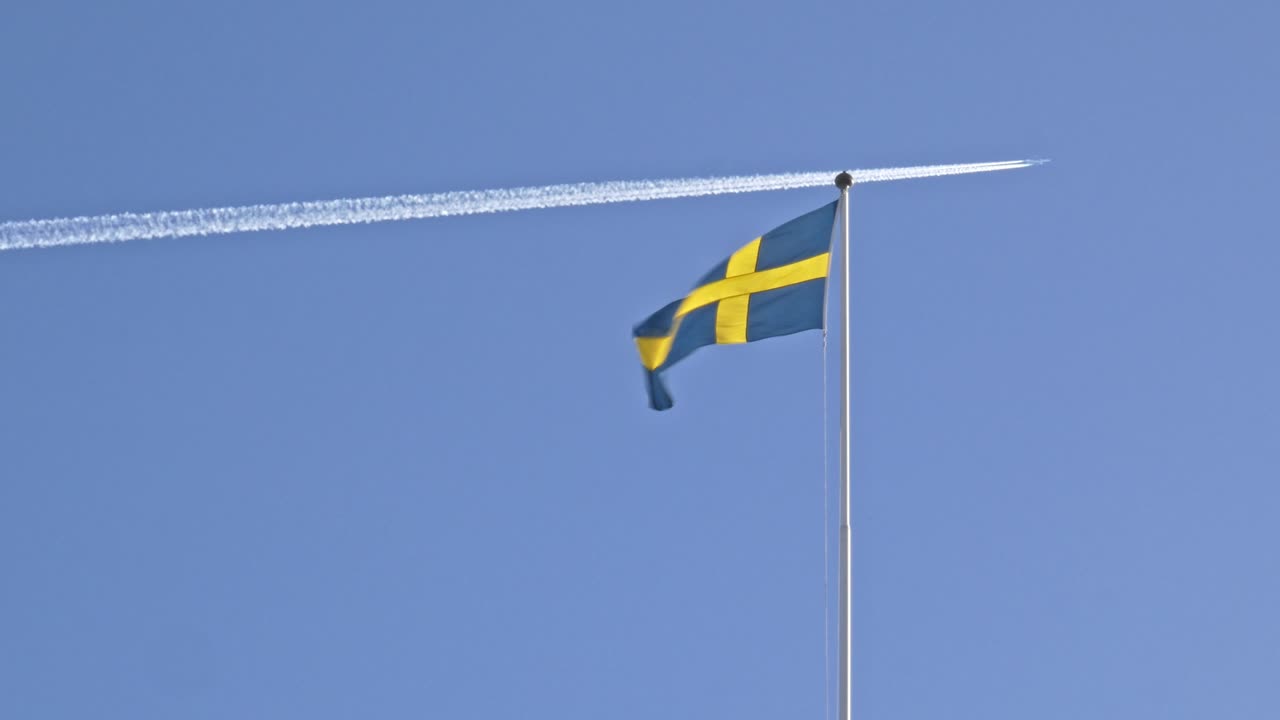 비행기가 배경에서 날아가는 동안 바람에 흔들리는 스웨덴 국기