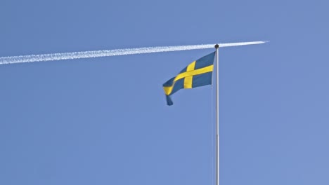 swedish flag waving on the wind while plane flies in the background