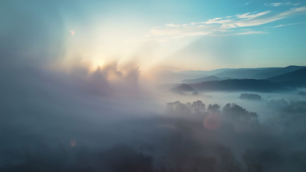 Gliding camera revealing misty forested valley at sunrise, capturing sunbeams, lens flare and hills