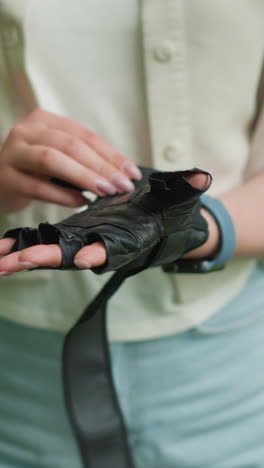 primer plano de una mujer con guantes negros con foco en las manos y un reloj inteligente en la muñeca derecha, rodeada de un paisaje verde borroso y pistas de caminos al aire libre