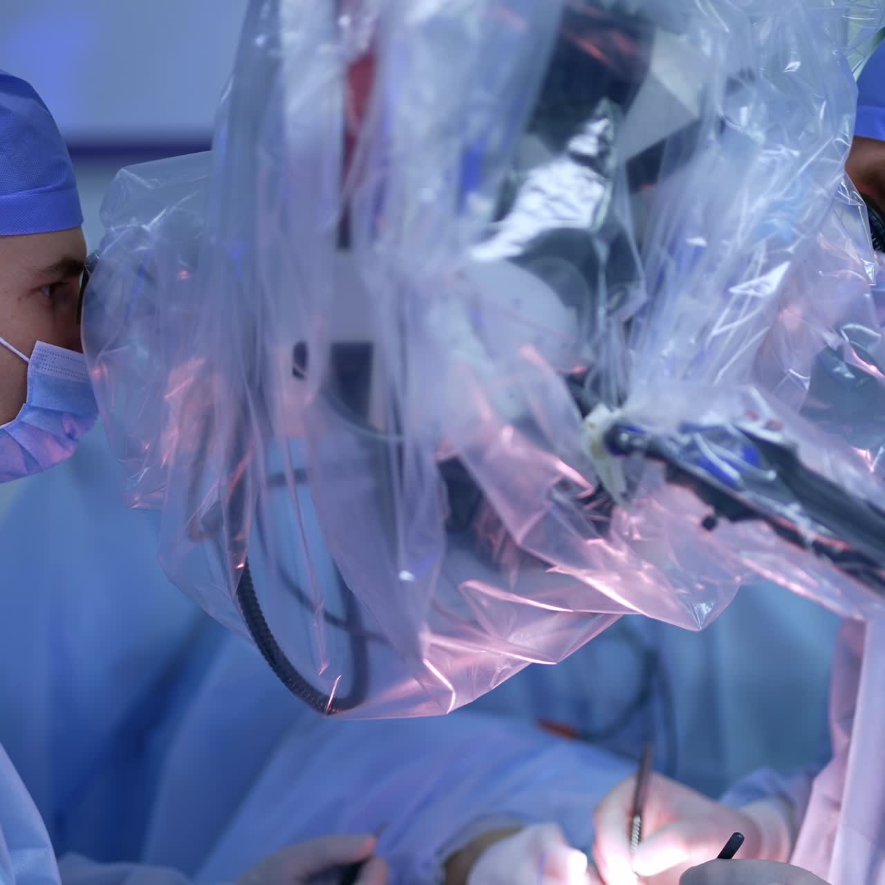 Male surgeons look at the operated area through the microscope. Doctors stand on both sides of equipment covered with plastic