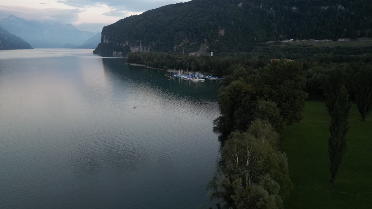 Aerial footage of Walensee's shoreline with silver-blue waters and a couple of sailboats docked in the small marina