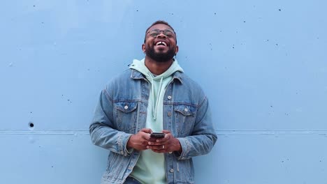 cheerful black man browsing smartphone near wall