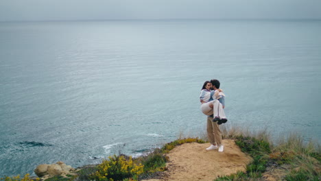 Loving-man-carrying-girlfriend-on-hands-standing-at-sea-shore-gloomy-evening.