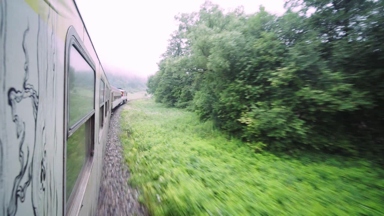 Hanging out of moving train, traveling through green forest in European mountains next to river, Slovakia