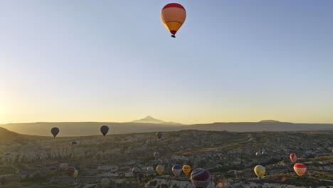 Göreme-Turkey-Aerial-V60-Filmischer-Flug-Hoch-über-Der-Stadt-Und-Um-Einen-Heißluftballon-Herum,-Der-Eine-Wunderschöne-Goldene-Sonnenaufgangslandschaft-Mit-Vulkanischen-Felsformationen-Einfängt---Aufgenommen-Mit-Mavic-3-Cine---Juli-2022