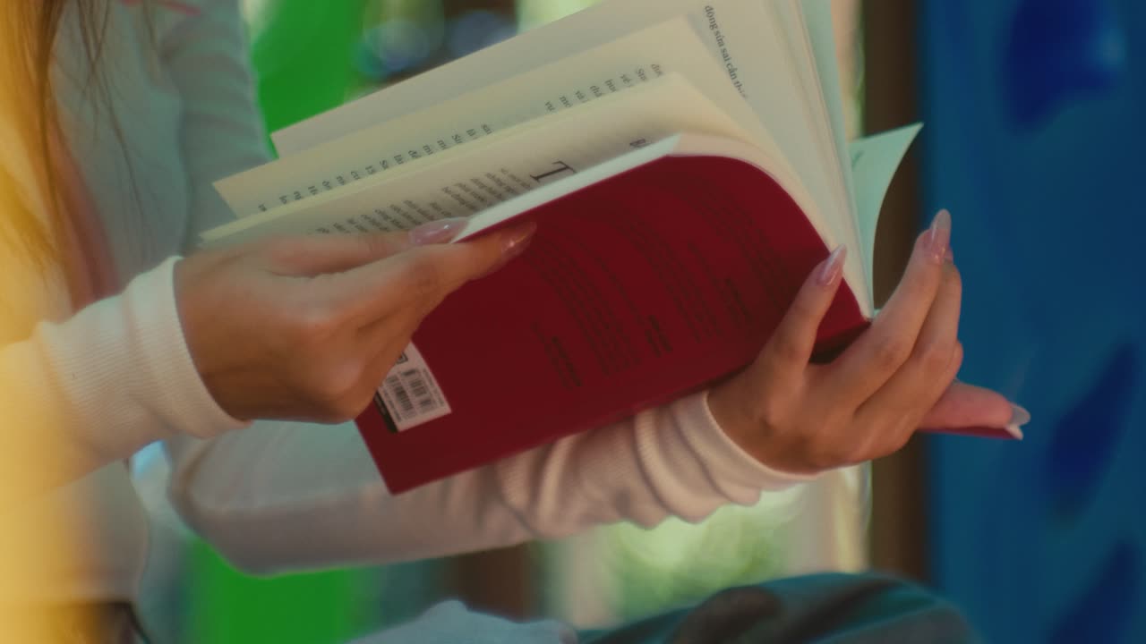 la cámara revela manos femeninas de cerca mientras da la vuelta a las páginas de un libro de novela al aire libre en un parque durante un día soleado