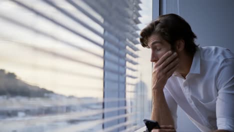 Front-view-of-young-Caucasian-male-executive-using-mobile-phone-near-window-in-modern-office-4k