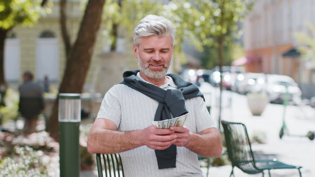 Rich happy mature man counting money income earnings cash calculate banknotes salary on city street