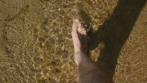 man walks on transparent water of a shallow lake during summer