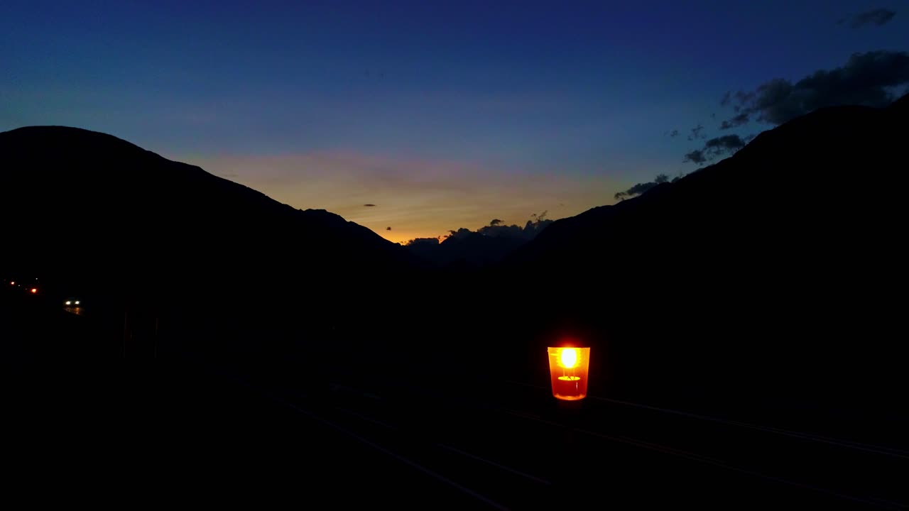 Quiet mountain road with glowing single lantern, car headlights passing by