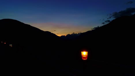 quiet mountain road with glowing single lantern, car headlights passing by