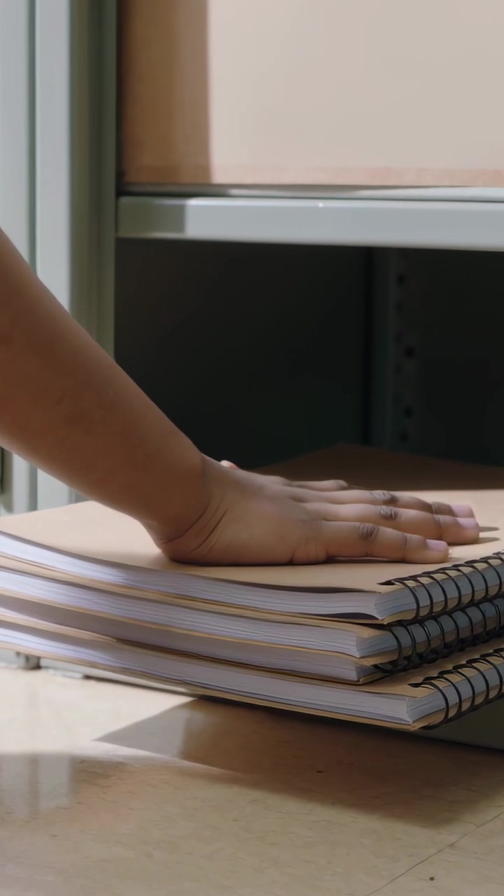 Video verticale: Mano che scorre da sinistra spostando quaderni sulla scrivania sotto una mensola di metallo, allineandoli ordinatamente.