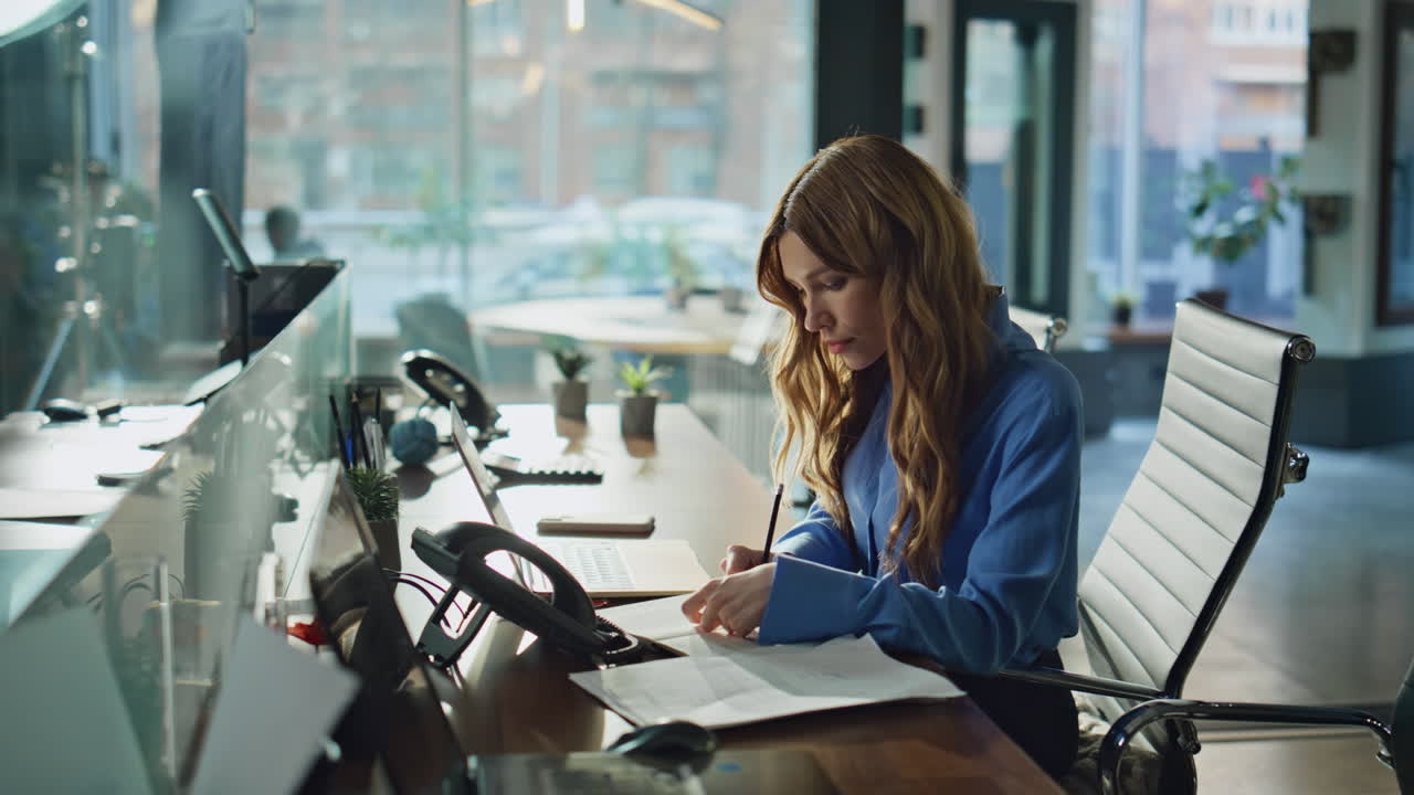 Focused professional working laptop at office desk writing notes in notebook