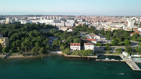 Zadar-Costero-De-Verano-Con-Drones,-Deslícese-A-Lo-Largo-De-La-Costa-Con-Piscina-Y-Ciudad-De-Plataforma-De-Buceo-En-El-Fondo