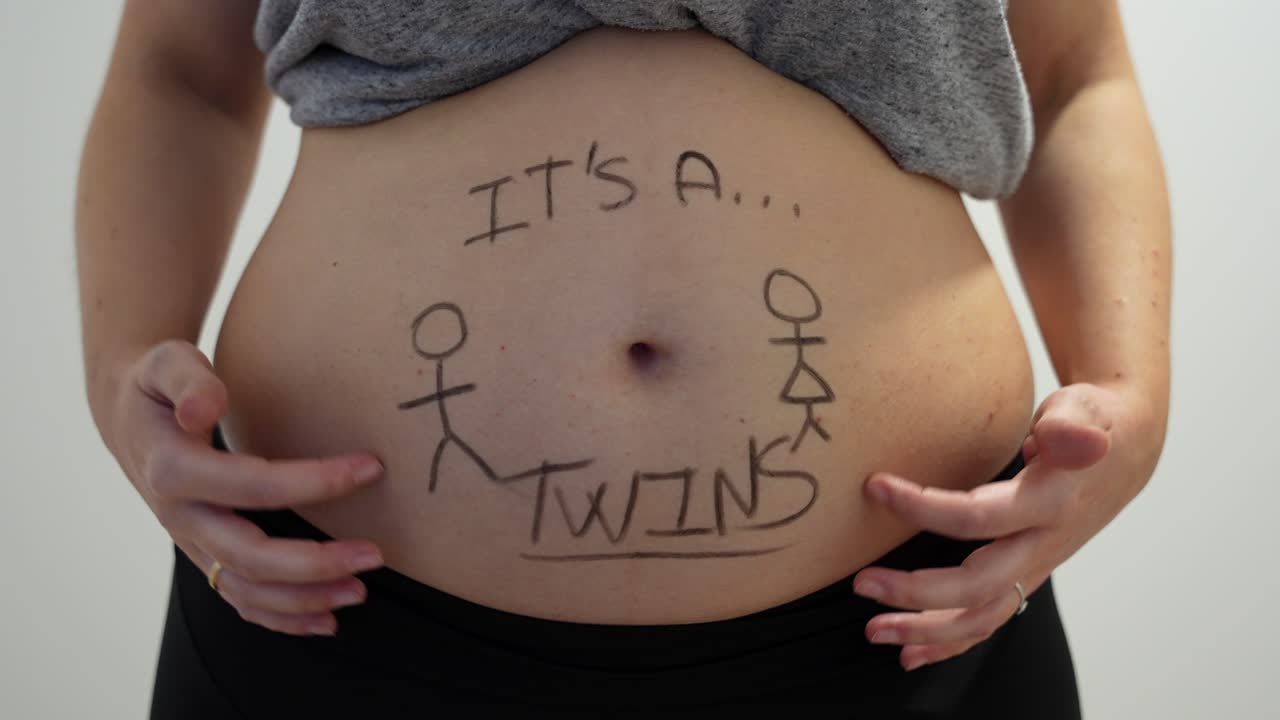 Close up of belly moving with "It's twins" written on with black marker. Pregnancy, 4K