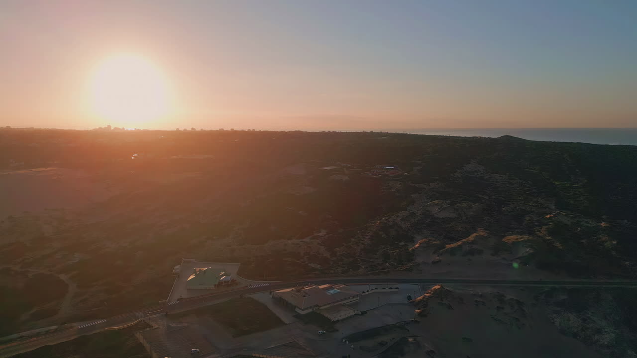 Sunset casting orange glow over landscape aerial view. Roadway distant buildings