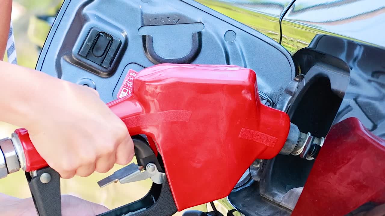 A person's hand holds a bright red fuel nozzle while refueling a modern car outdoors