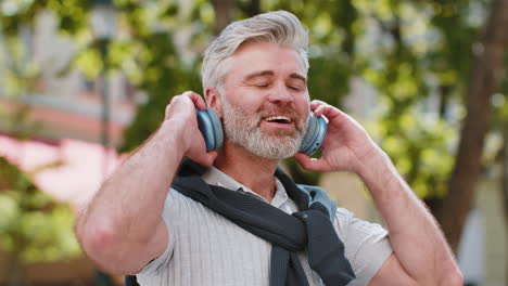 relaxed smiling mature bearded man listening energetic disco rock n roll music dancing outdoors