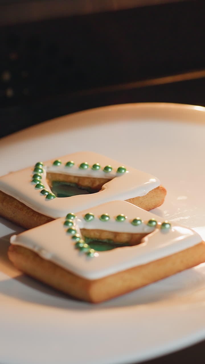 오븐 안의 색 접시에 색 아이싱과 녹색 설탕 진주를 가진 두 개의 아름답게 장식된 쿠키의 클로즈업, 따뜻한 노란색 오븐 빛에 의해 조명