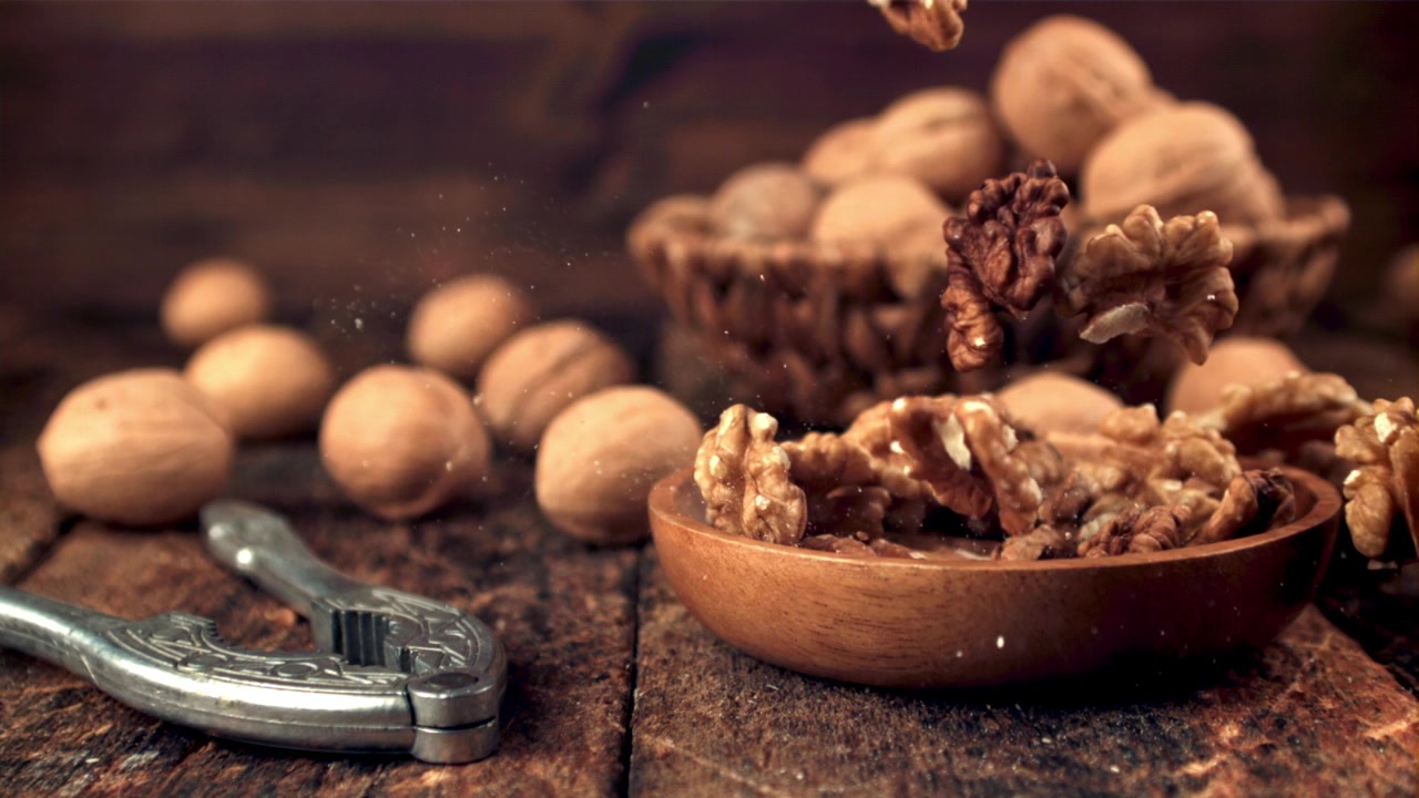 Shelled Walnuts Falling into a Wooden Bowl on a Rustic Table