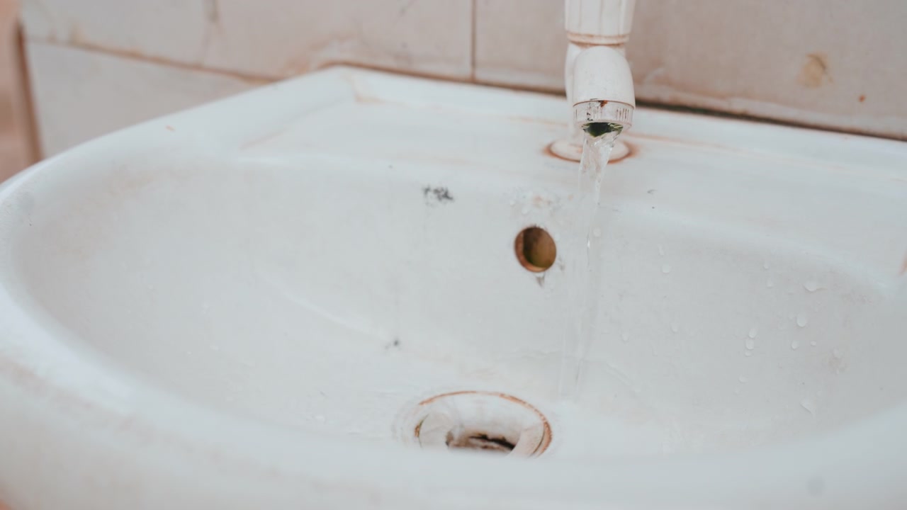 Korozyonlu eski seramik lavabo. Yaşını ve ihmalkar terk edilmişliğini gösteren paslanmış seramik evye. Uzun süreli ihmali ve belirgin çürüme belirtilerini yansıtan hasarlı ve korozyonlu lavabo