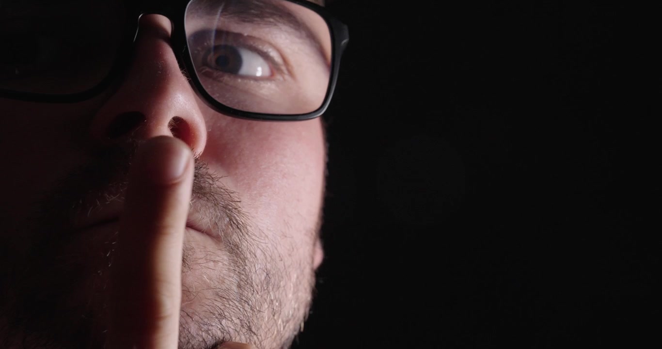 Close-up of a thoughtful man in a dark setting, touching his chin while thinking, representing decision making, reflection, and problem solving.