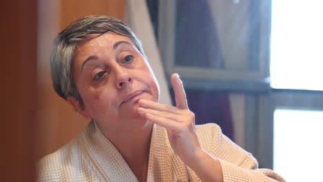 mujer mayor en bata de baño aplicando crema facial