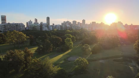 Aerial-dolly-right-of-Municipal-golf-course-in-Palermo-neighborhood-with-buildings-in-background-at-sunset,-Buenos-Aires