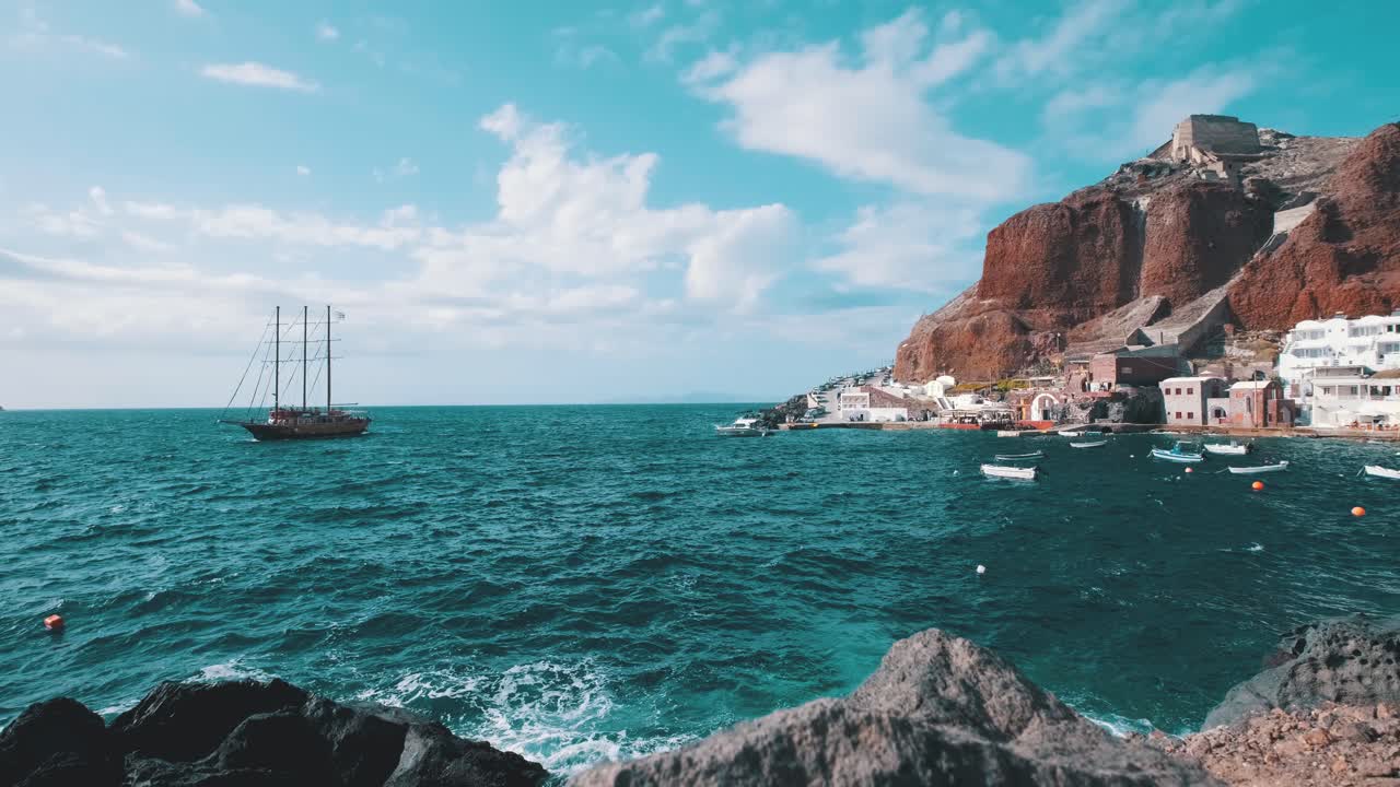 gran velero de madera frente a un pequeño pueblo de cala en santorini