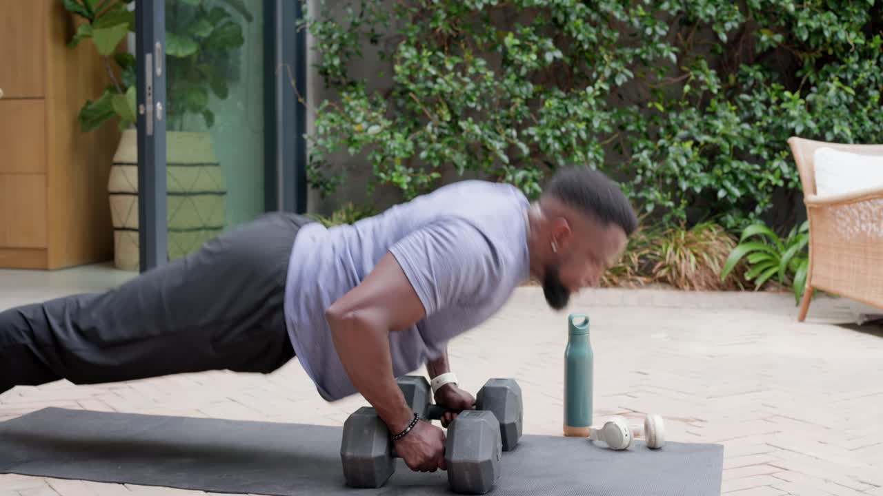 Man gripping dumbbells doing pushups on mat shifting into pike and kneeling, stretching for fitness