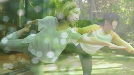 animation of glowing spots over asian mother and daughter exercising in garden