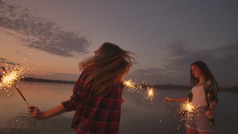 A-group-of-friends-girls-and-men-dance-on-the-beach-with-sparklers-in-slow-motion-at-sunset.-Celebrate-new-year-on-the-beach