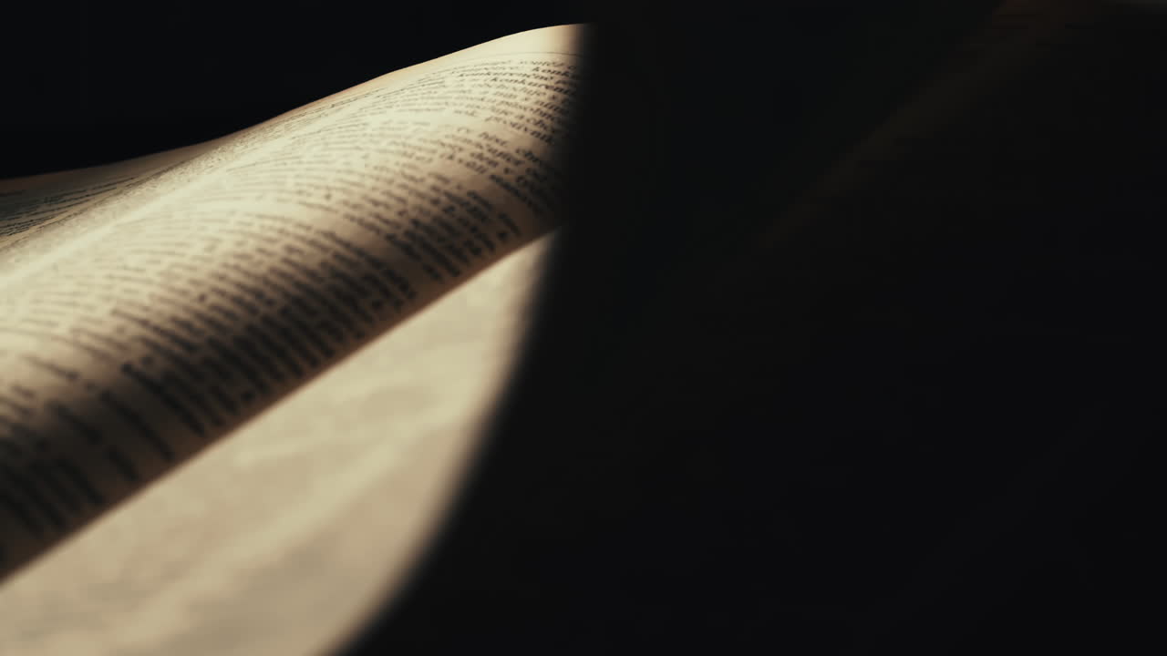 Una mano gira drammaticamente pagina in un vecchio libro in una stanza buia, primo piano.